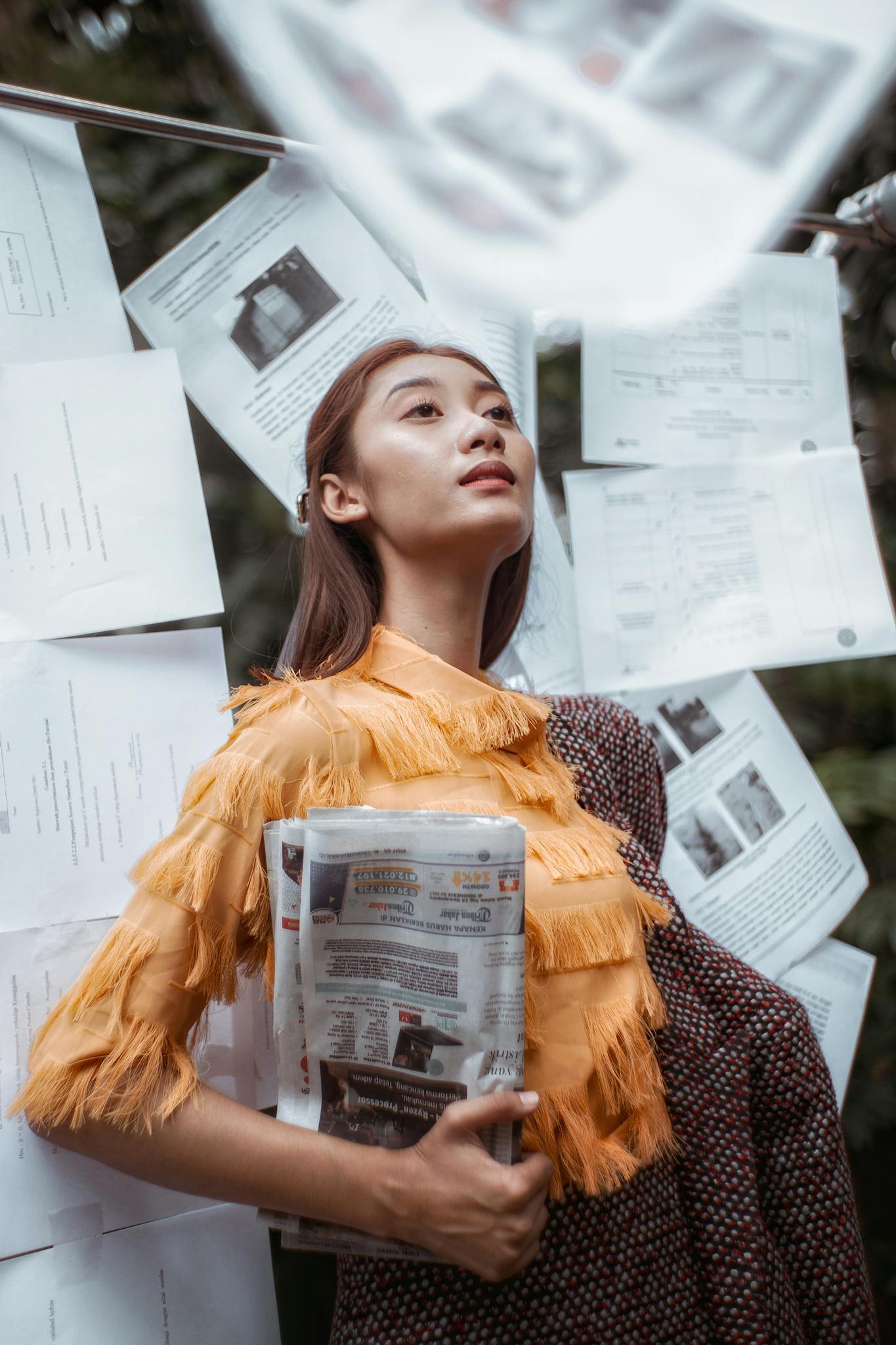 Fashionable woman posing with newspaper and documents hanging outdoors, exuding confidence.
